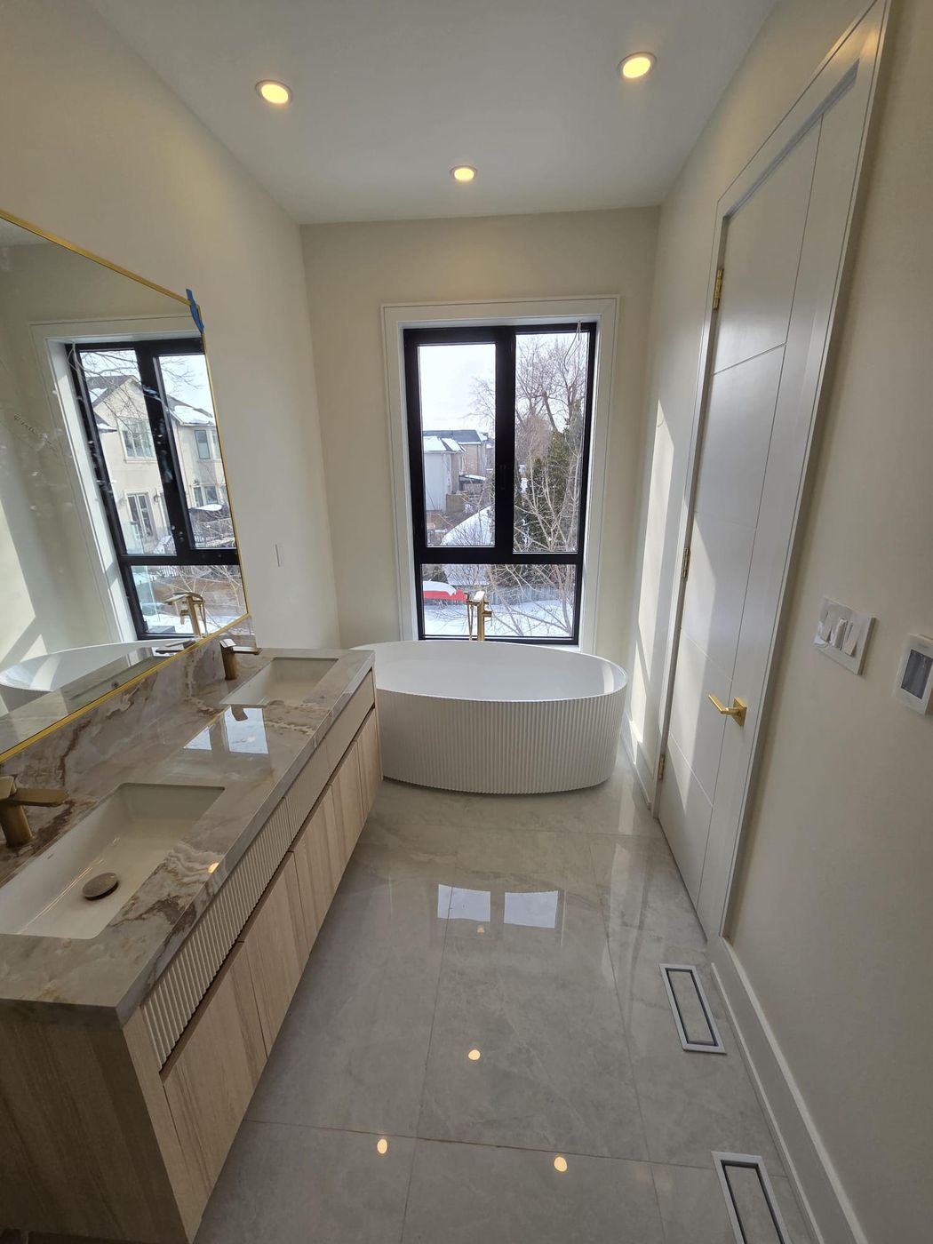 Bright ensuite with a fluted freestanding tub, floor-mounted gold tub filler and a double vanity with gold faucets