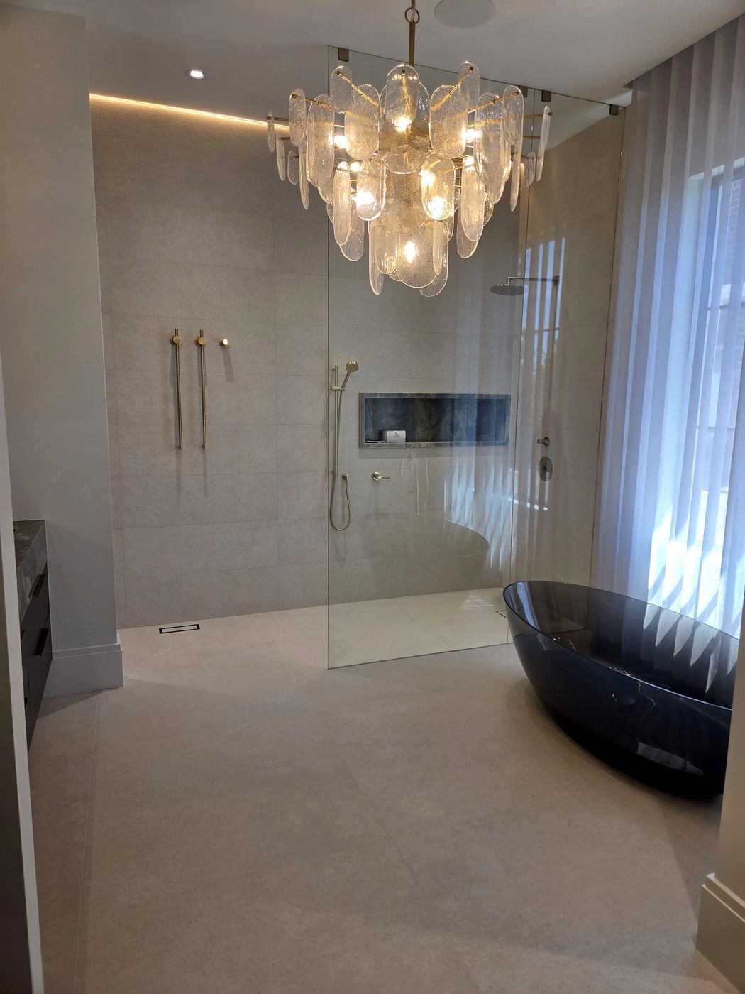 Luxury ensuite with a smoked-glass freestanding tub, crystal chandelier and a curbless walk-in shower with brushed-gold fixtures